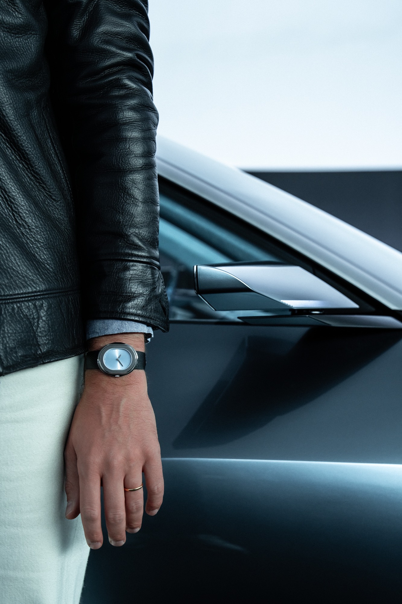 The Serica Parade Bleu Glacier worn on the wrist in front of the concept car